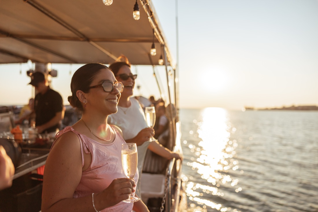 Guests with drinks on the covered deck of Cape Adieu at sunset on Darwin Harbour