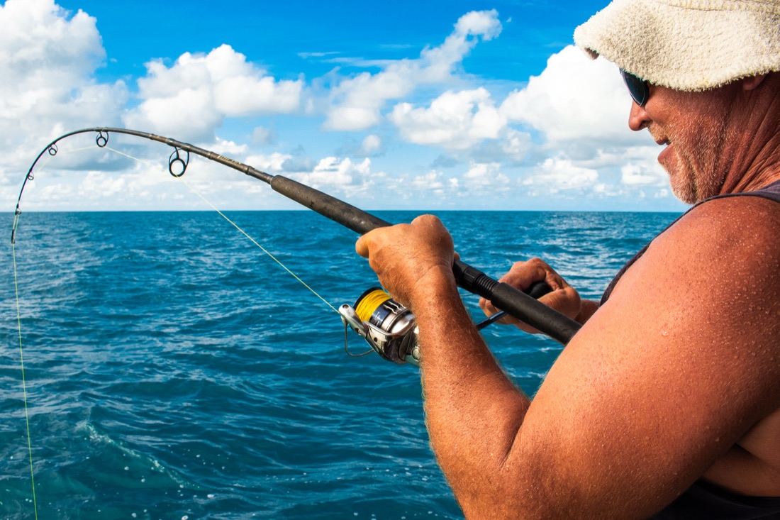 Angler working a hooked fish on a full-day offshore fishing charter out of Darwin